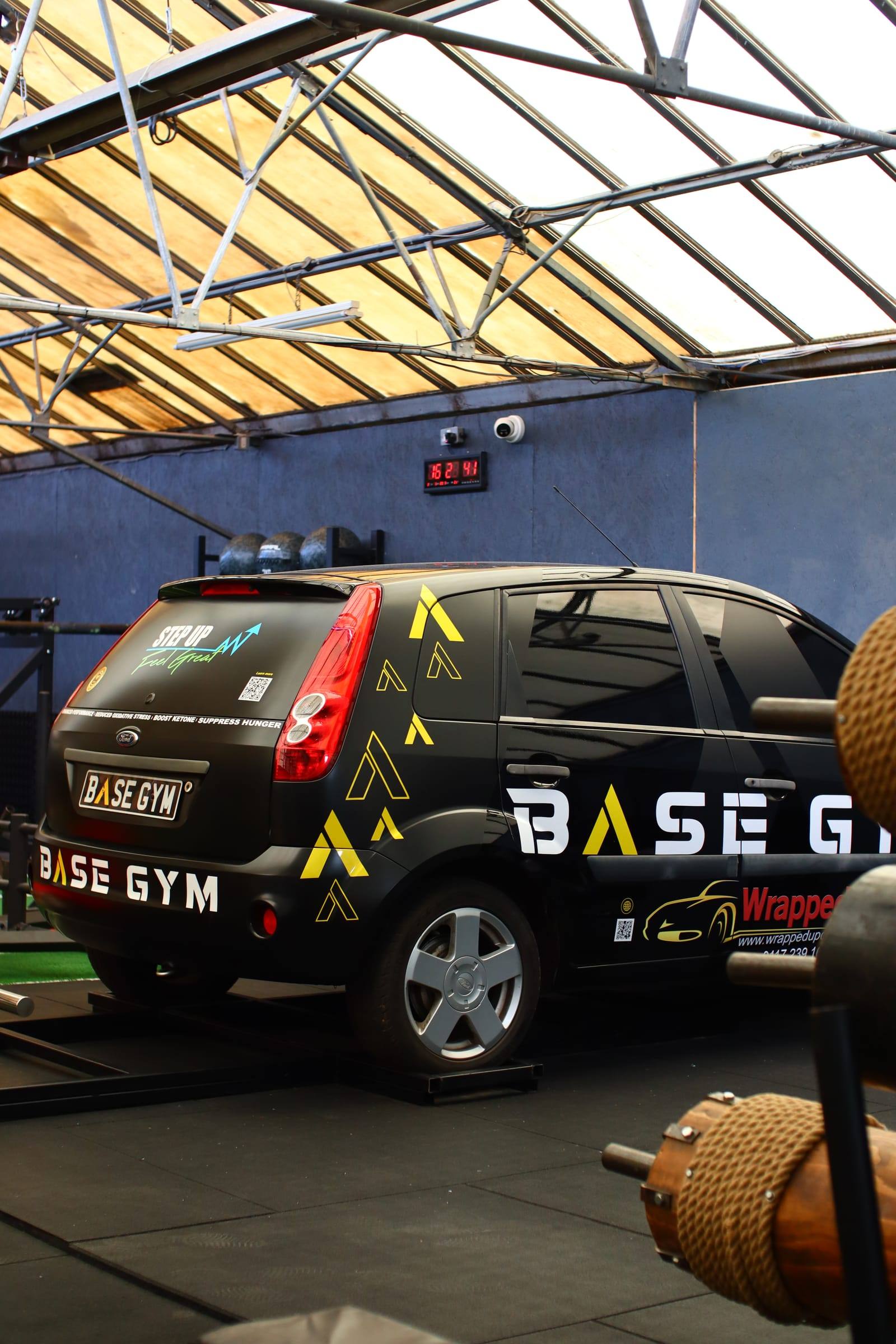 Base Gym branded car set on a deadlift frame beside a strongman log at the Bristol gym